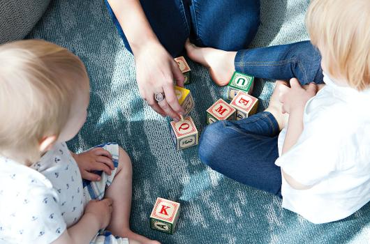 一个成人和两个孩子在地板上玩字母块