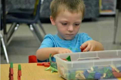 小男孩排序块在学校书桌用塑料箱的构建块在他的面前