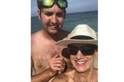 一个母子站在海洋前进行自拍照。儿子的头顶上有绿色的Google，他的妈妈有一顶白色的草帽，正在微笑。他们俩都在微笑