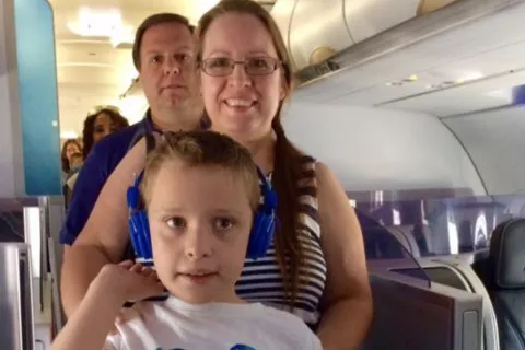 一个男孩和他的爸爸妈妈登上飞机，男孩戴着蓝色耳机